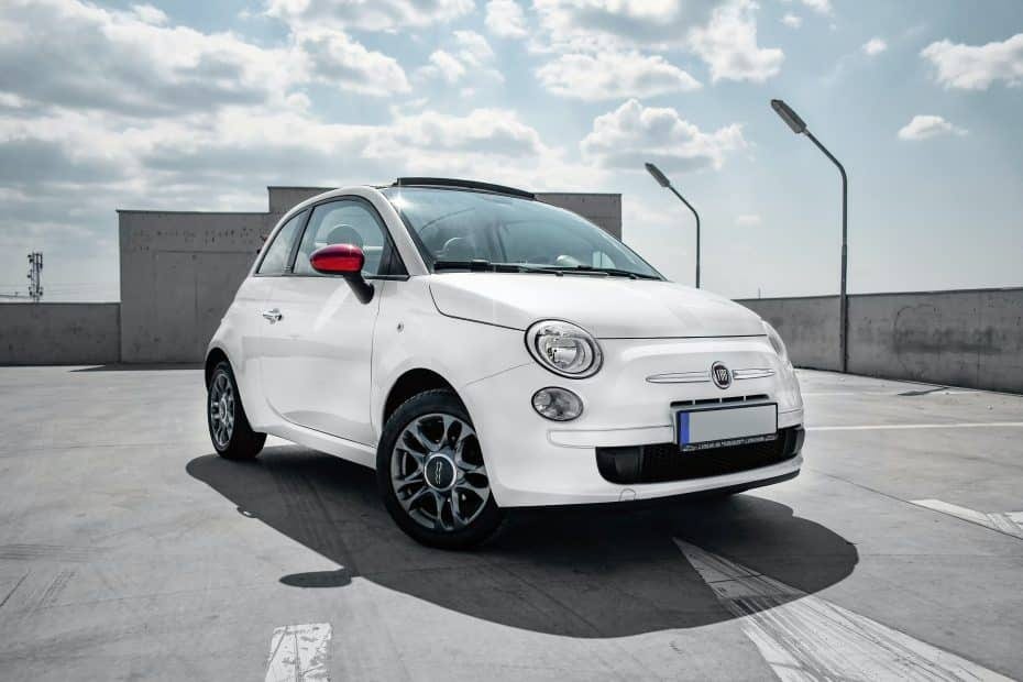 A white fiat 500 is parked in a parking lot.