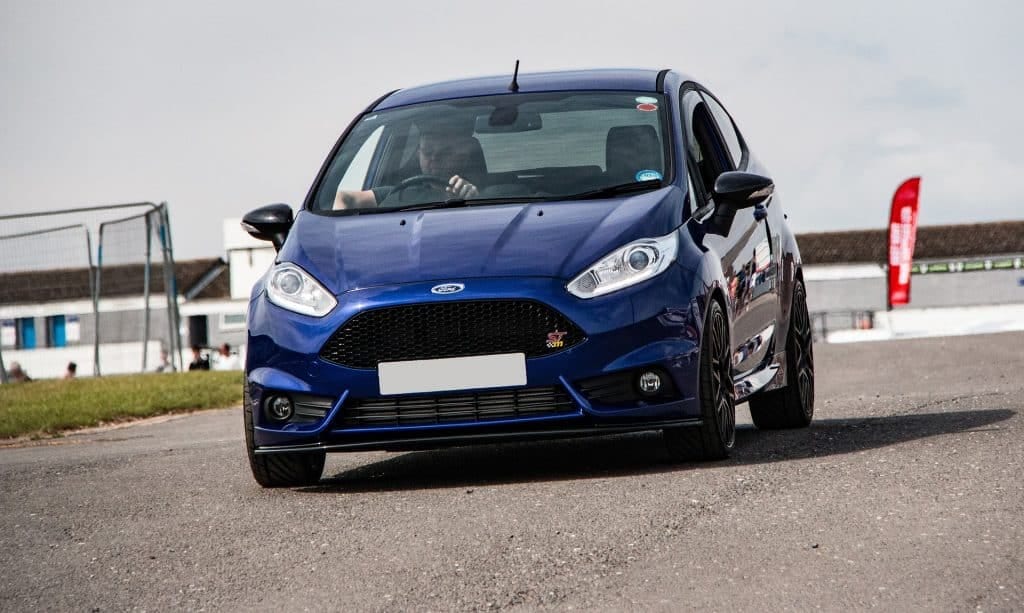 A blue ford fiesta st driving down a race track.