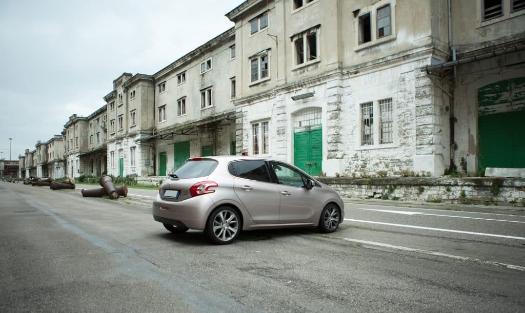 A Peugeot 208 is parked on a street in front of an old building.