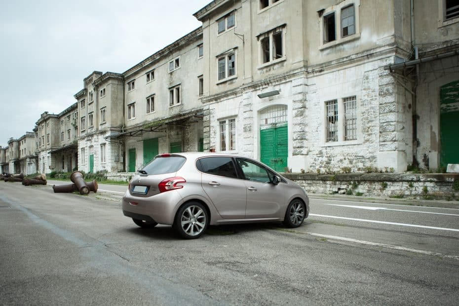 A Peugeot 208 is parked on a street in front of an old building.