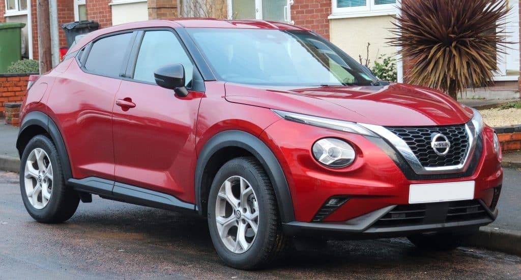 The red nissan juke is parked on the side of the road.