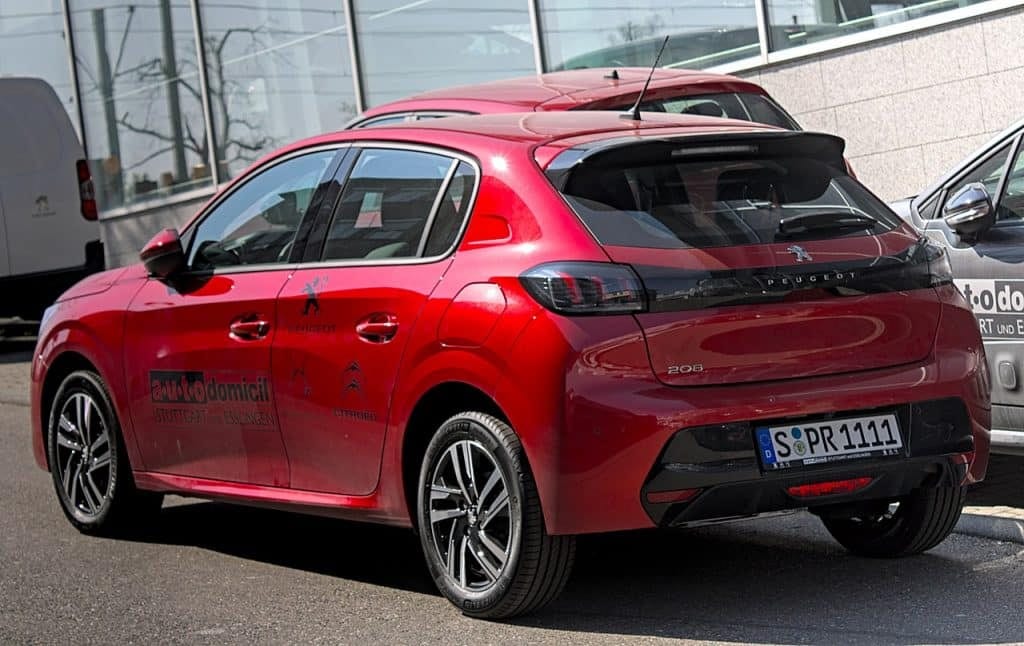 A red Peugeot 208 parked in front of a building.