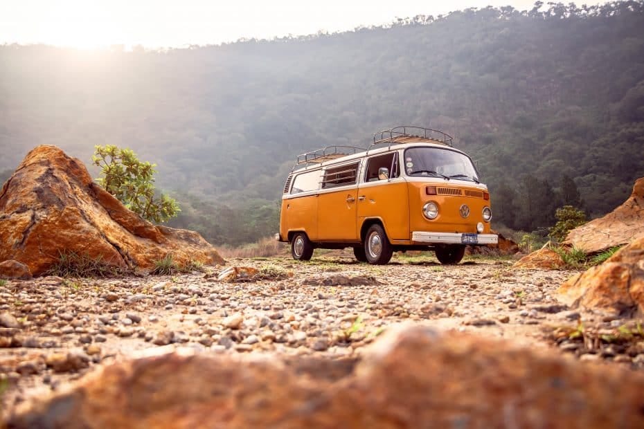 An orange vw bus parked on a dirt road.