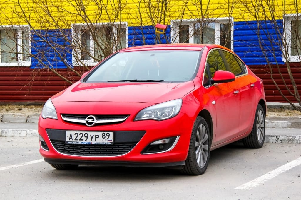 A red car parked in front of a colorful building.