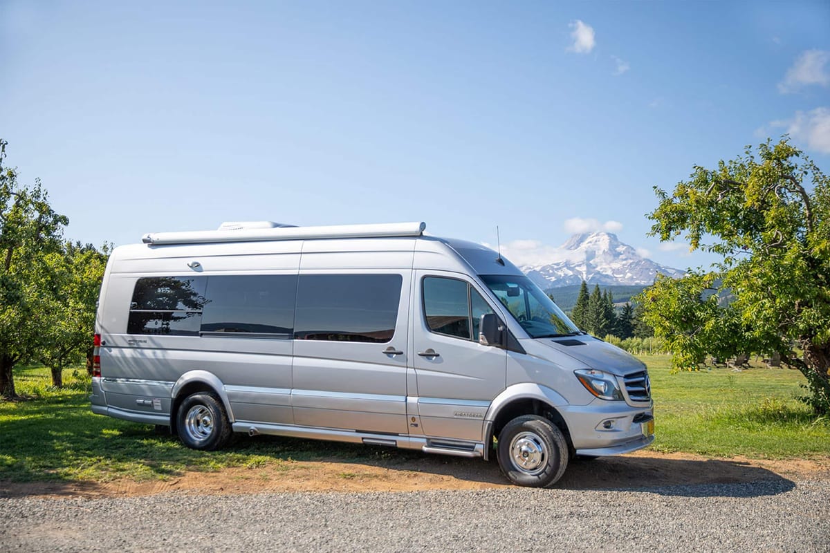 A silver mercedes - benz sprinter parked in front of a mountain.